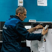 Un tecnico concentrato in uniforme blu ripara un elettrodomestico in un ambiente interno.